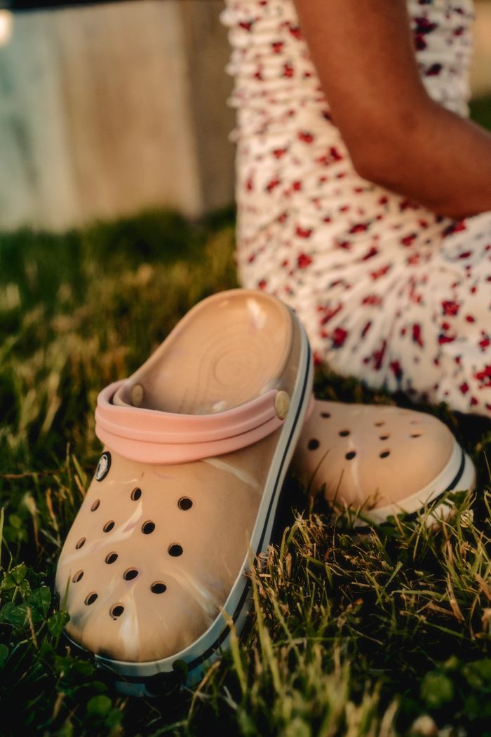 Contact Close-up of casual beige clogs on grass, perfect for summer fashion.