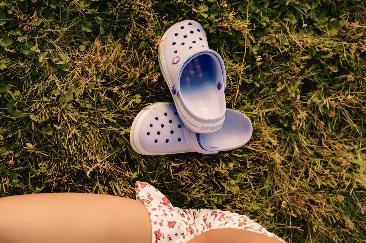 About Purple crocs and floral dress on green grass, embodying summer leisure.