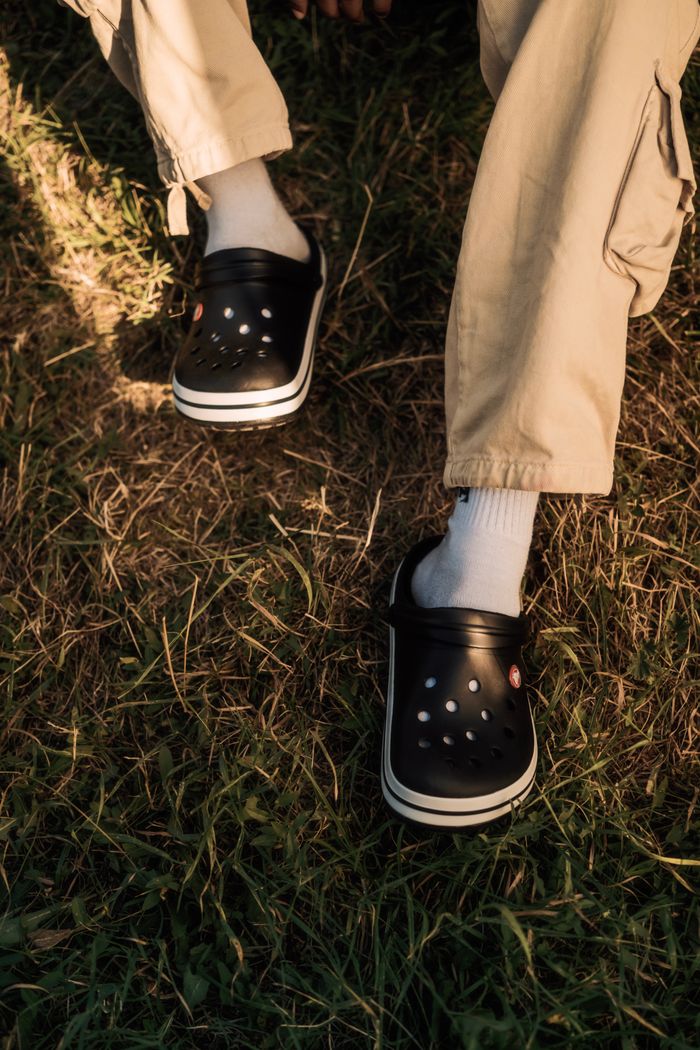 About Casual black clogs paired with white socks and khaki pants on a grassy field.
