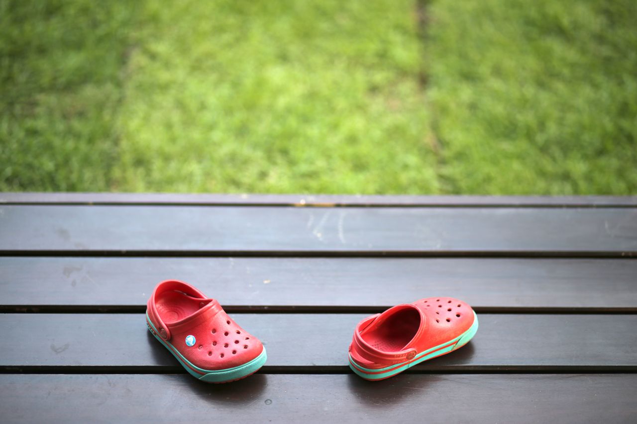 Pair of red shoes on a wooden bench with green grass background in a garden.