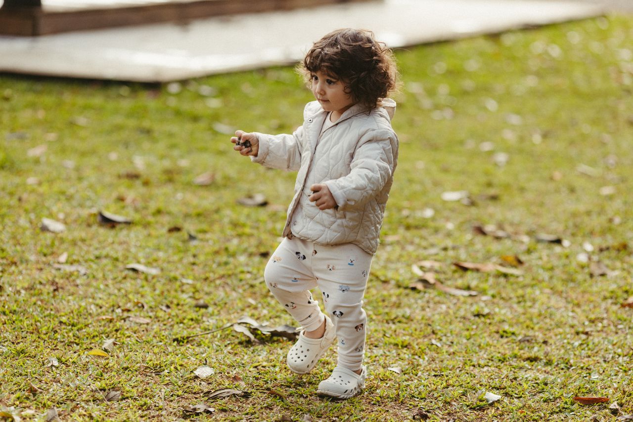 About A cute toddler in a jacket walking on the grass in an outdoor park during fall.